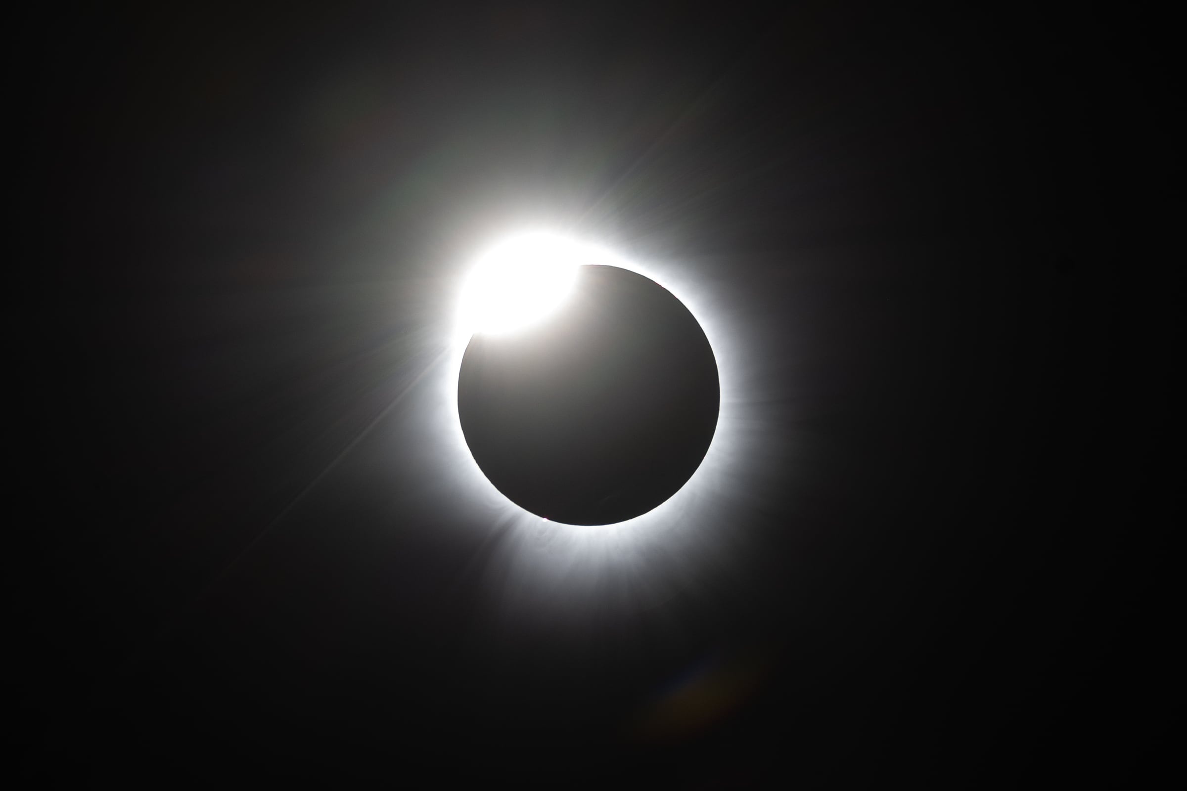 The black disk of a total solar eclipse is ringed by a white corona and a bright diamond of sunlight.