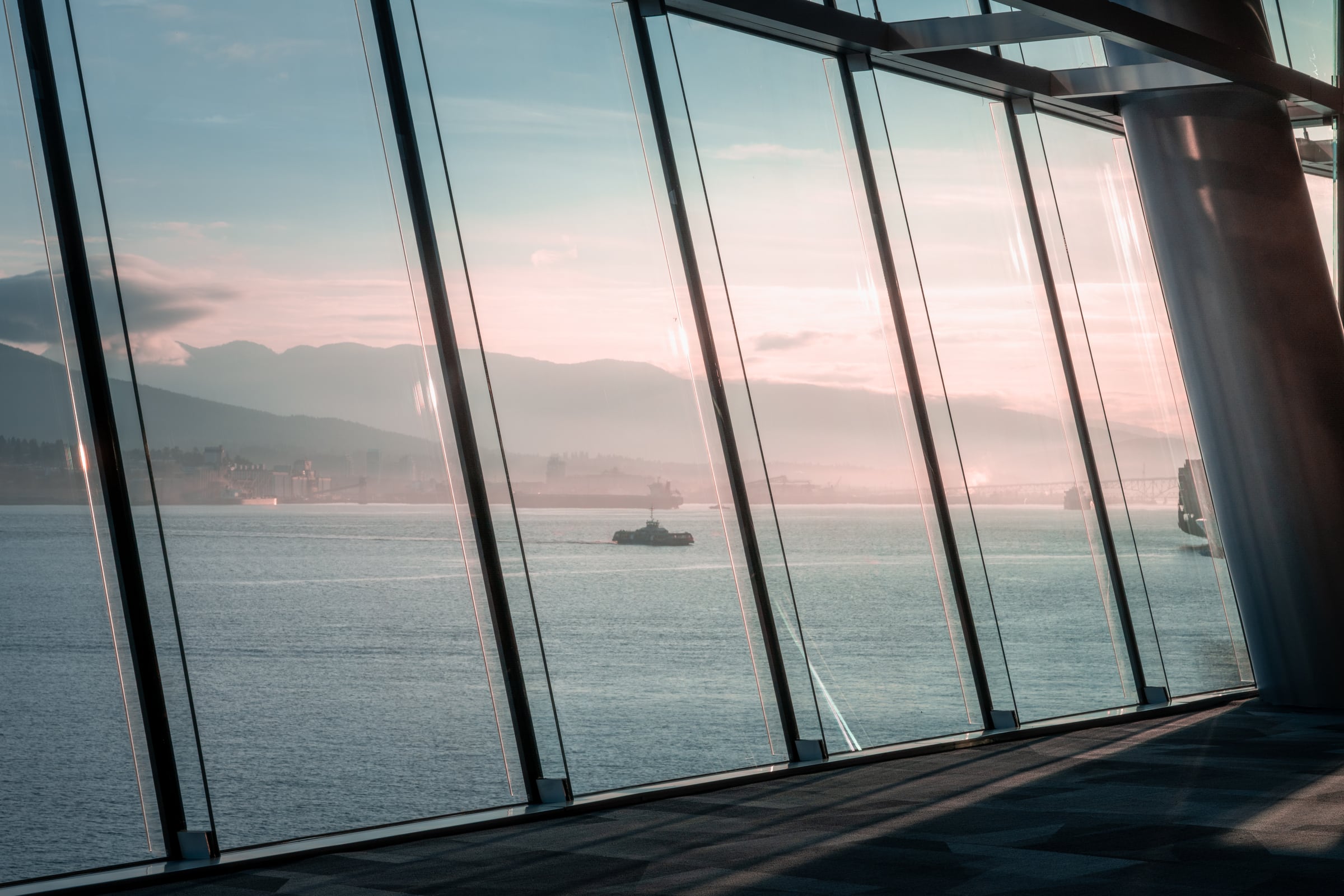 Floor-to-ceiling windows frame a hazy waterfront and mountains in pale morning light.